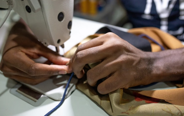 A person's hand guides thread through the needle of a sewing machine during setup.
